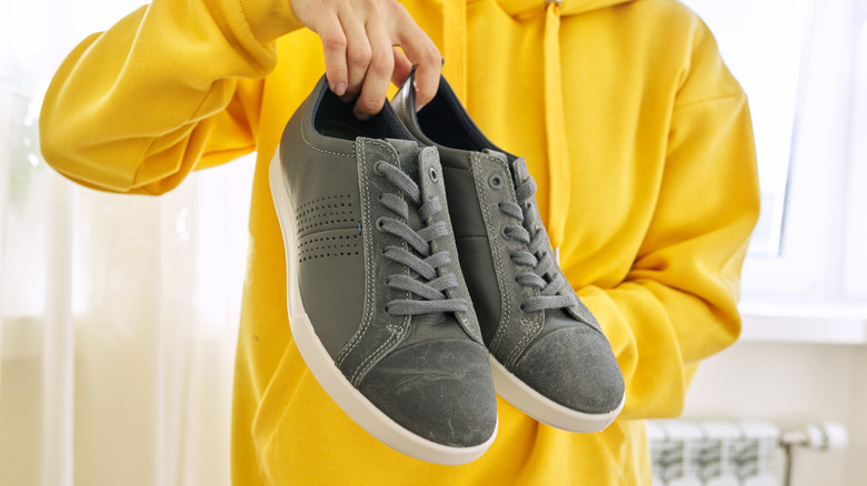 Person in yellow sweatshirt holding pair of shoes