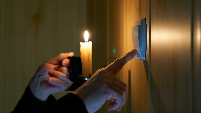 A person holding a candle while turning the light switch on