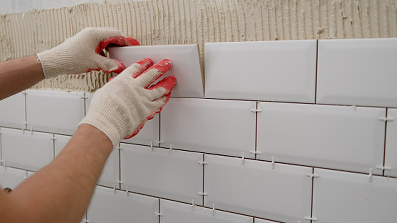 A person installing white subway tile backsplash in a kitchen
