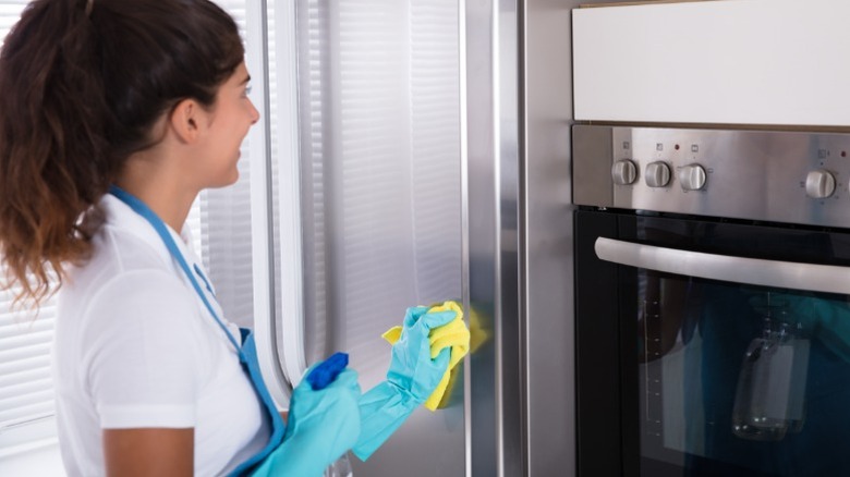 Person cleaning stainless steel refrigerator with club soda spray and cloth