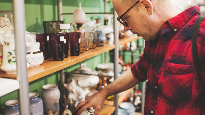 A man looks at glassware on the shelves of a thrift store