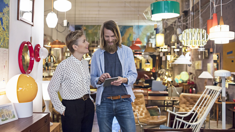 A couple smiles in a thrift store surrounded by unique lighting