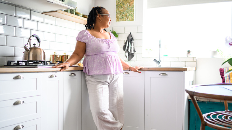 A woman standing in a small, cluttered kitchen