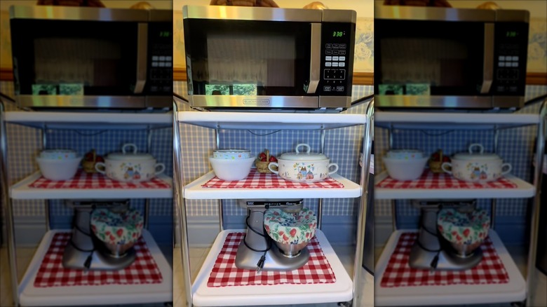 Bar cart used as kitchen storage cart with microwave, dishes, and stand mixer on shelves
