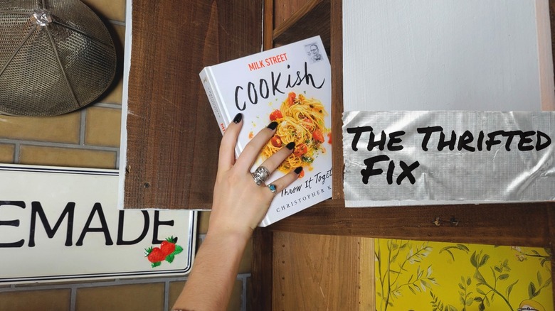 Hand reaching pulling a cookbook from thrifted countertop cabinet