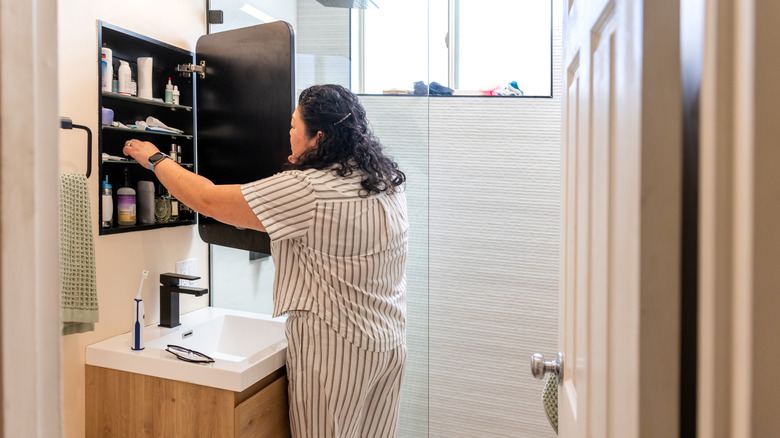 A person looking for an item in a bathroom medicine cabinet
