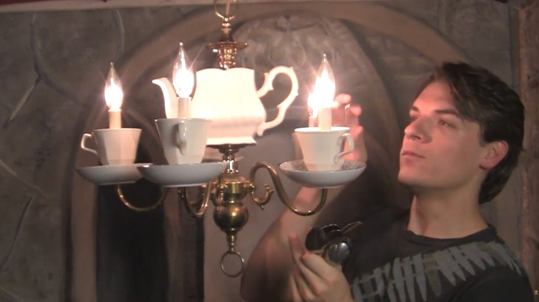 Person decorating teacup chandelier with lit lights