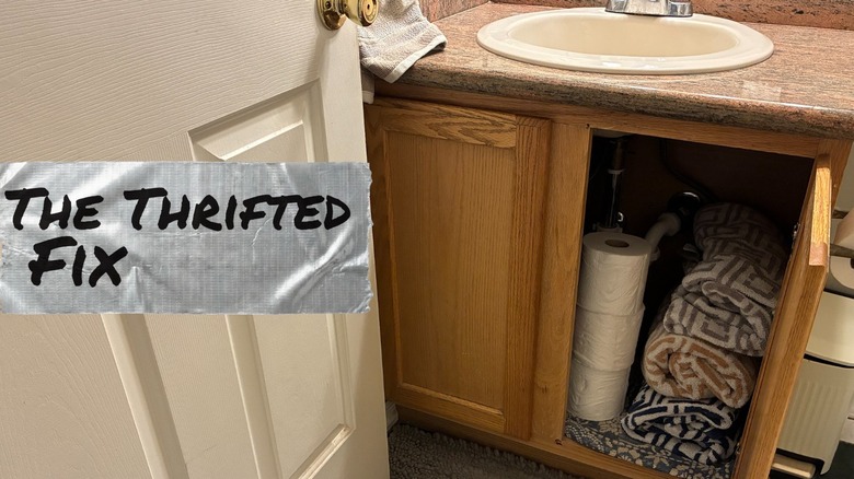 Small bathroom with open cabinet filled with toilet paper and towels