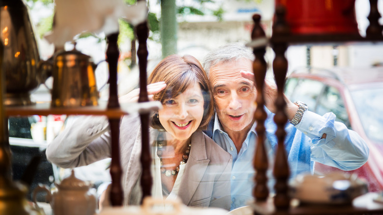 A couple smiles as they look in the window of an antique furniture shop