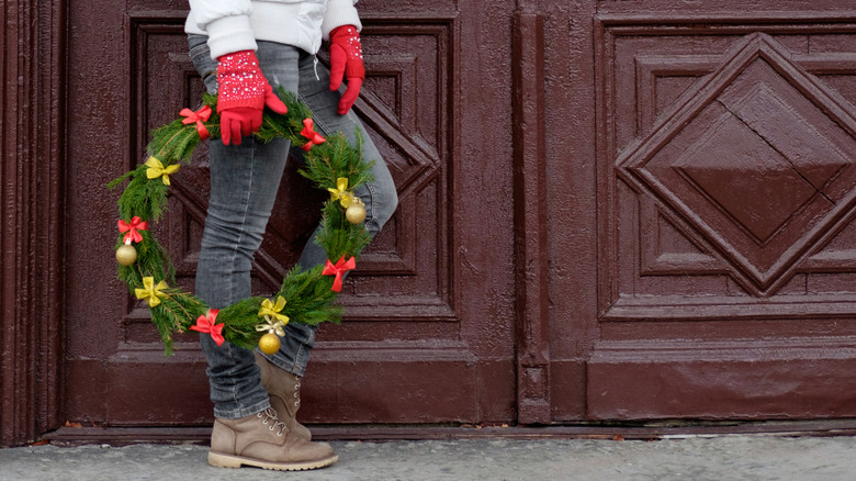 A person standing in front of a double door holding a traditional wreath in their gloved hand