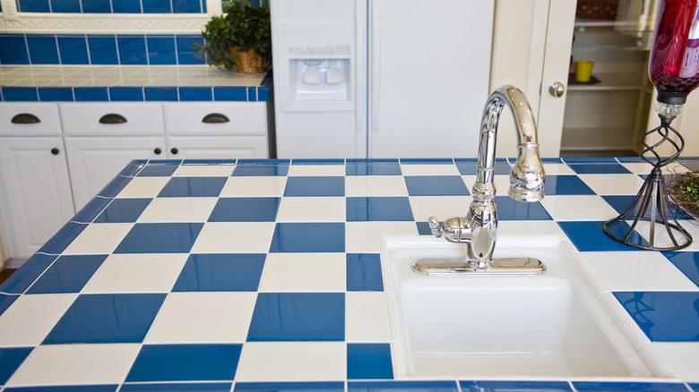 A dated kitchen features blue and white tile countertops