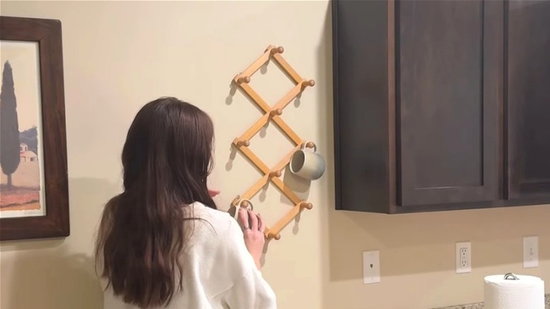 Woman using thrifted accordion rack as kitchen organizer for mugs