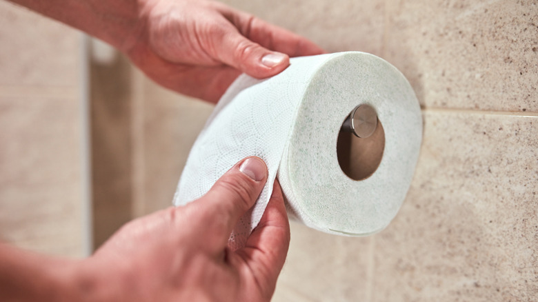 Man ripping off piece of toilet paper in bathroom