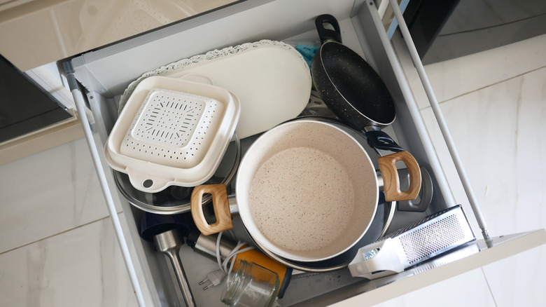 cluttered kitchen drawer with pots and pans and other kitchen items