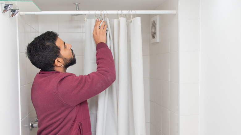 Person adjusting shower curtain in small white-tiled shower.