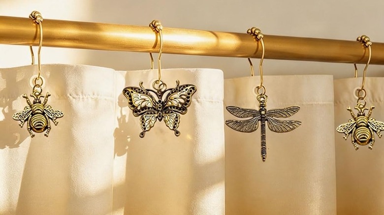 Gojidiy Dragonfly, Butterfly, and Bee Curtain Rings on gold curtain rod in front of beige shower curtain.