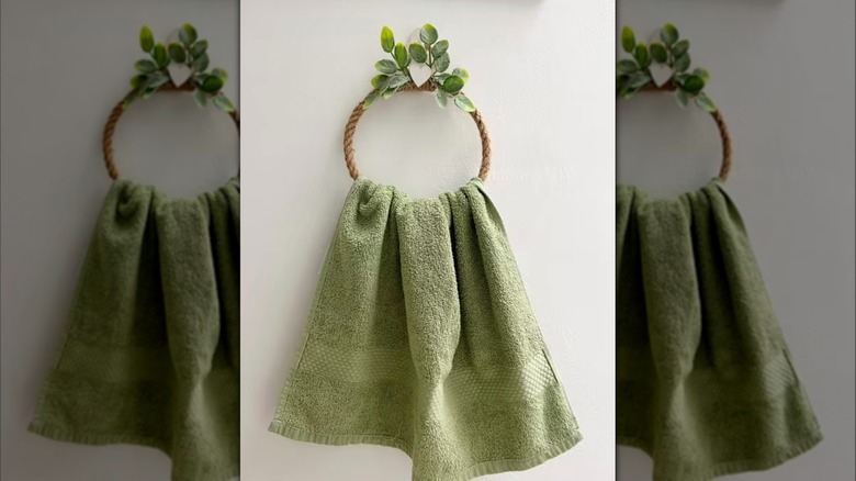 A green towel on a rope towel ring with faux foliage attached to the top