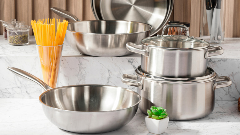 stainless steel cookware on a marble countertop against wooden wall