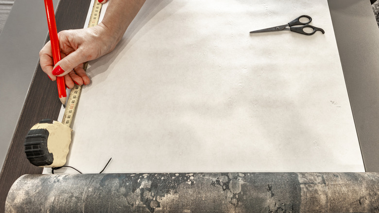 A person measuring wallpaper for cutting