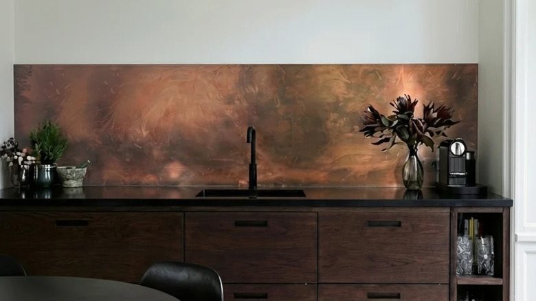 A modern kitchen with dark cabinetry and a copper sheet backsplash