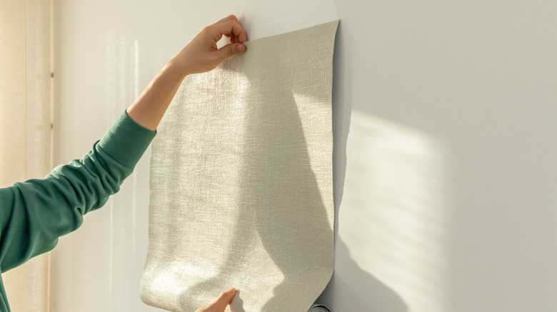 Person holding wallpaper up to the wall