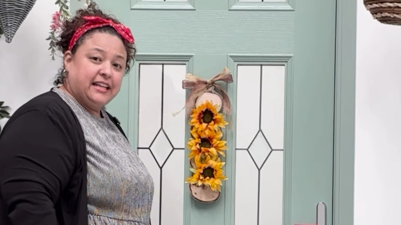 A person standing next to a fall-themed door decoration with sunflowers