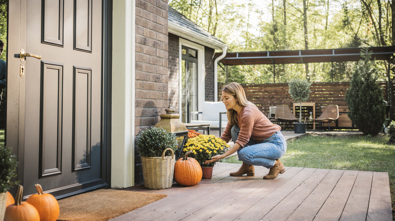 A young woman decorates a front porch with fall mums