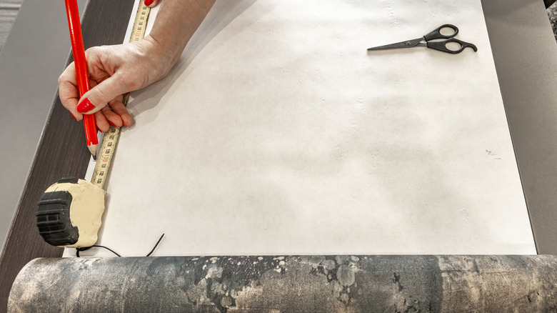 A person measuring wallpaper for cutting