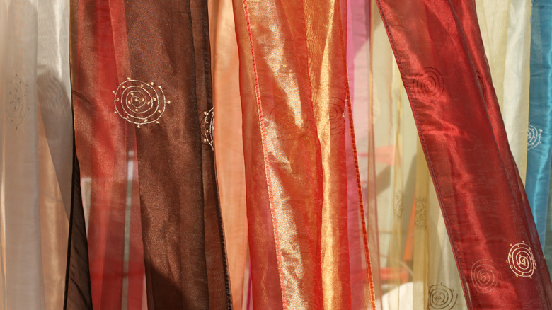 Long multicolored silk scarves hanging side by side in front of a window