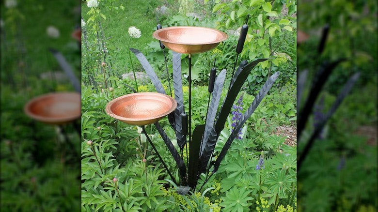 A naturalistic copper and iron birdbath is surrounded by lush green plants