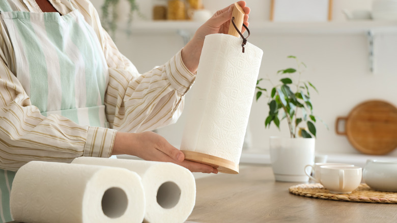 A person in a kitchen holding a traditional wooden paper towel holder