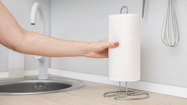 A person placing a roll of paper towels on a countertop holder.