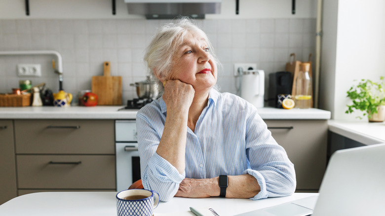Senior woman dreamily looking out kitchen window