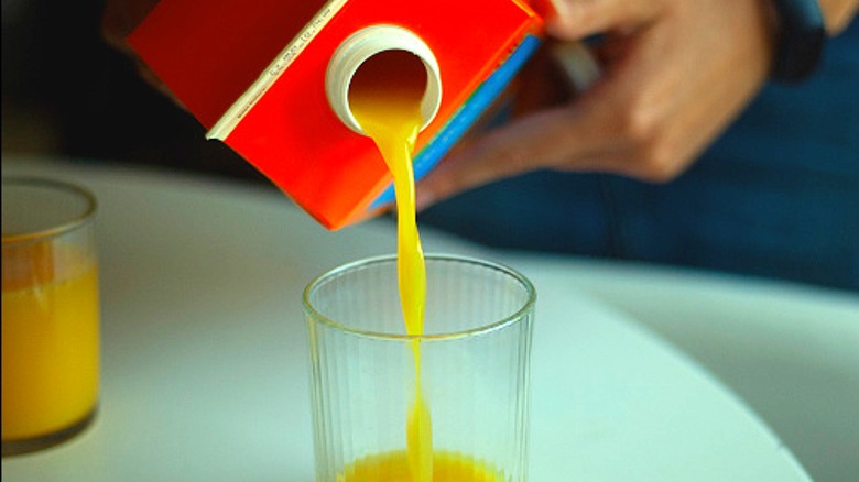 person pouring orange juice from carton