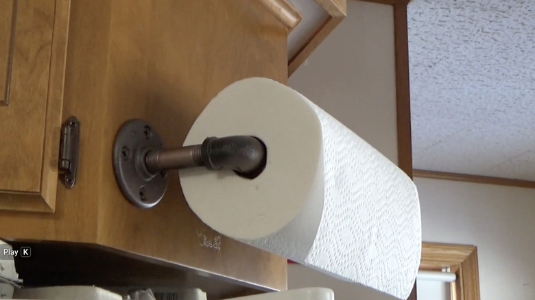 A roll of paper towels hangs from a DIY holder made from plumbing pipe and fittings