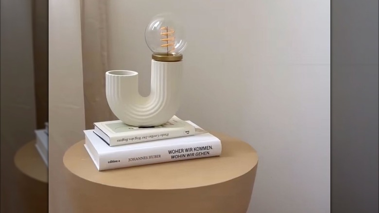 A modern lamp made using an IKEA hack rests on a stack of books sitting on top of a brown side table
