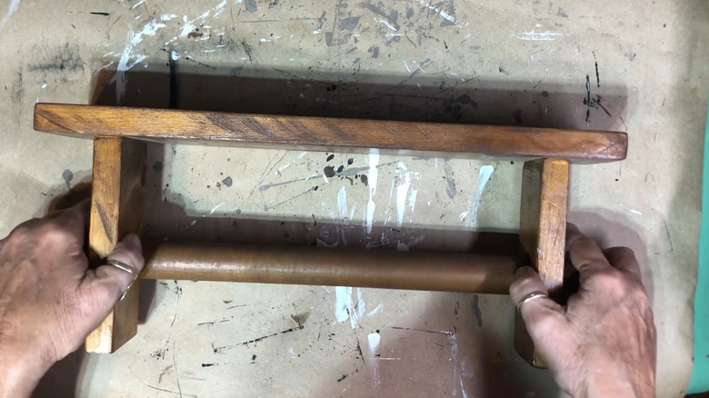 Person picking up a thrifted wood paper towel holder
