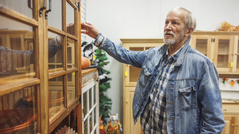 senior man looking at an old hutch with glass doors in thrift shop