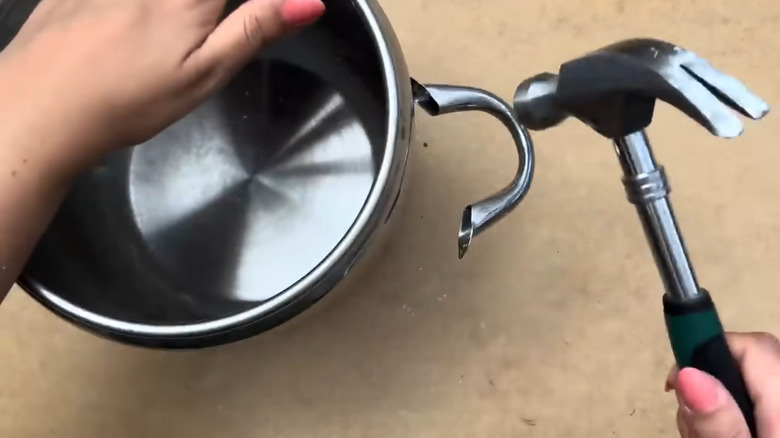 Person removing a broken handle off of a pot with a hammer