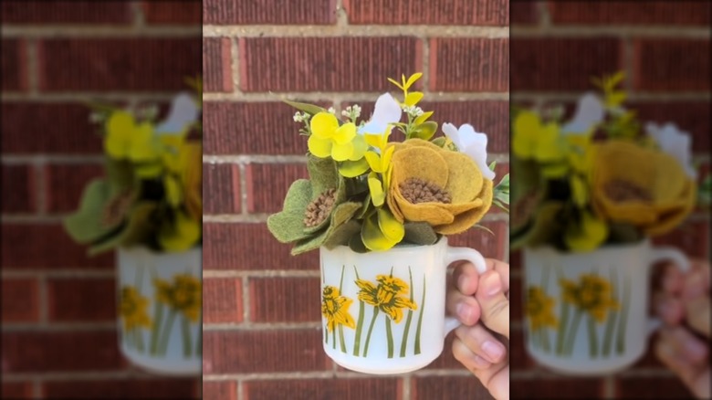 A vintage milk mug with yellow and green florals in front of a brick wall