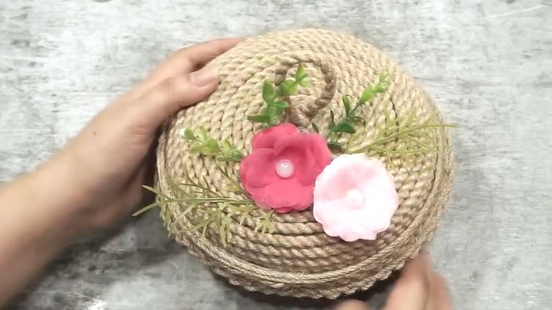 Round plastic takeout container covered in rope and floral decor as countertop organizer