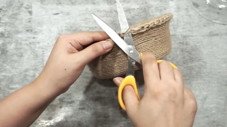 Hands trimming twine from burlap-wrapped takeout container for countertop DIY