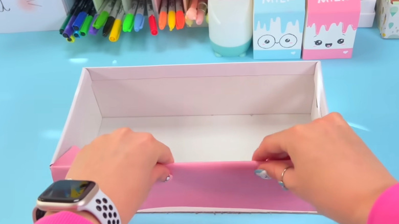 Hands cover a shoe box in pink contact paper in a cute room of colorful crafts