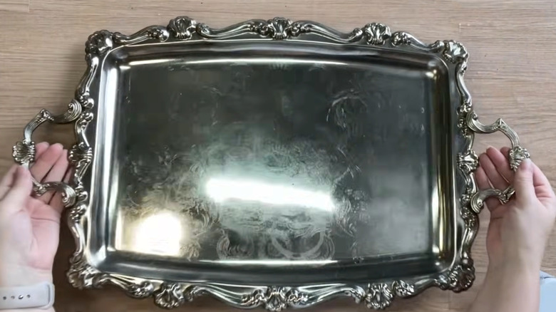 A woman prepares a vintage silver tray on a table