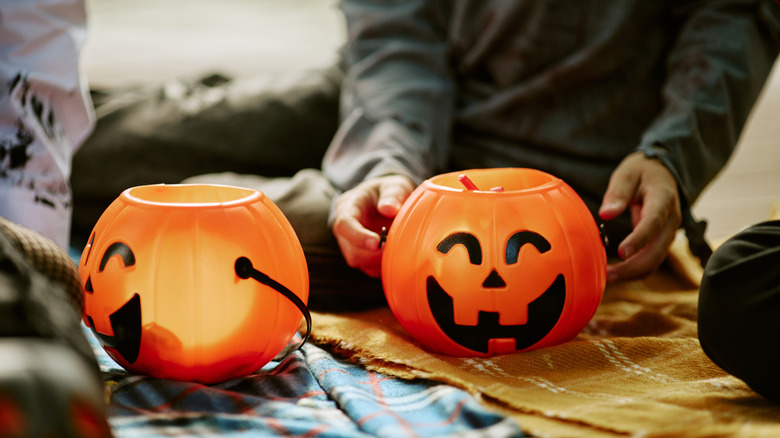 A person's hand in costume reaching for one of two plastic jack o lantern buckets
