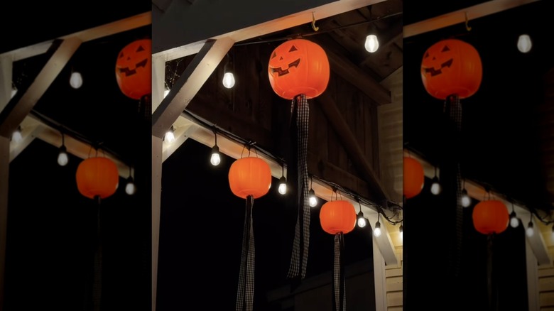 A nighttime shot of a porch with string lights and plastic jack o lantern buckets with ribbons