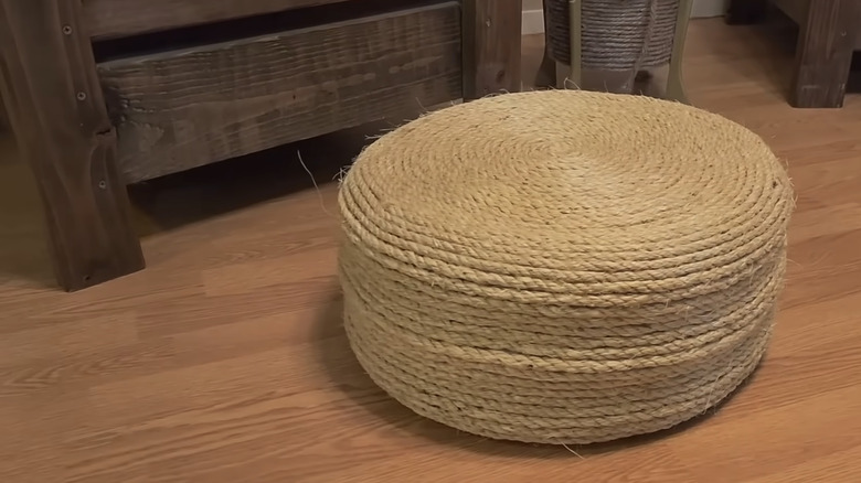 A natural twine-wrapped ottoman sits on a wooden floor in front of a chair