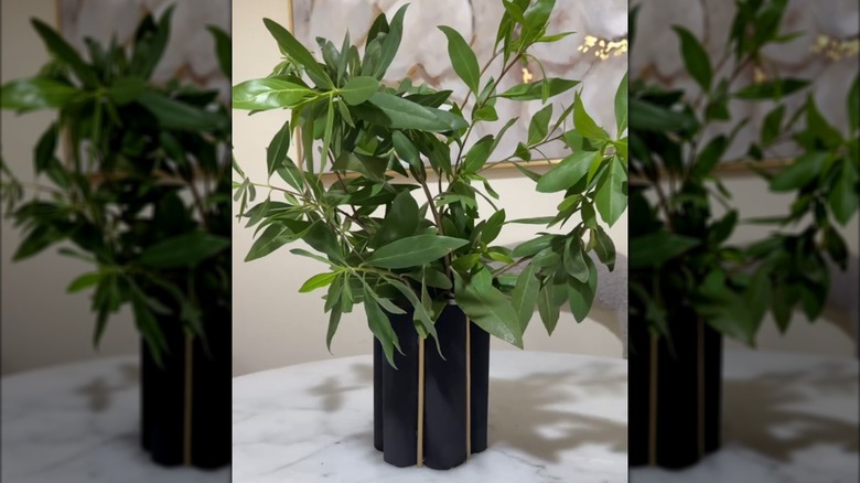 DIY black and gold paper tube vase with green leafy plants on white marbled table in elegant room