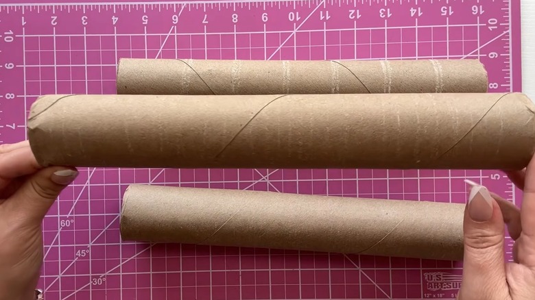 Hands holding multiple paper towel rolls over pink cutting mat