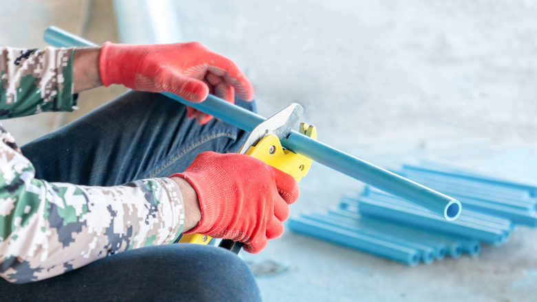 Person cutting PVC pipes using a yellow pipe cutter